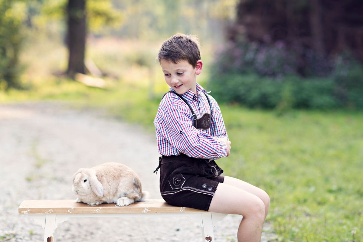Junge sitzt auf einer Bank und betrachtet ein Kaninchen waehrend eines outdoor Fotoshootings